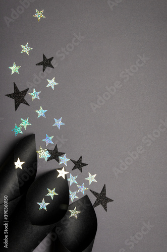 Vertical image.Abstract image of curled paper and shiny golden and black glitter stars on the grey surface.Empty space © uaPieceofCake