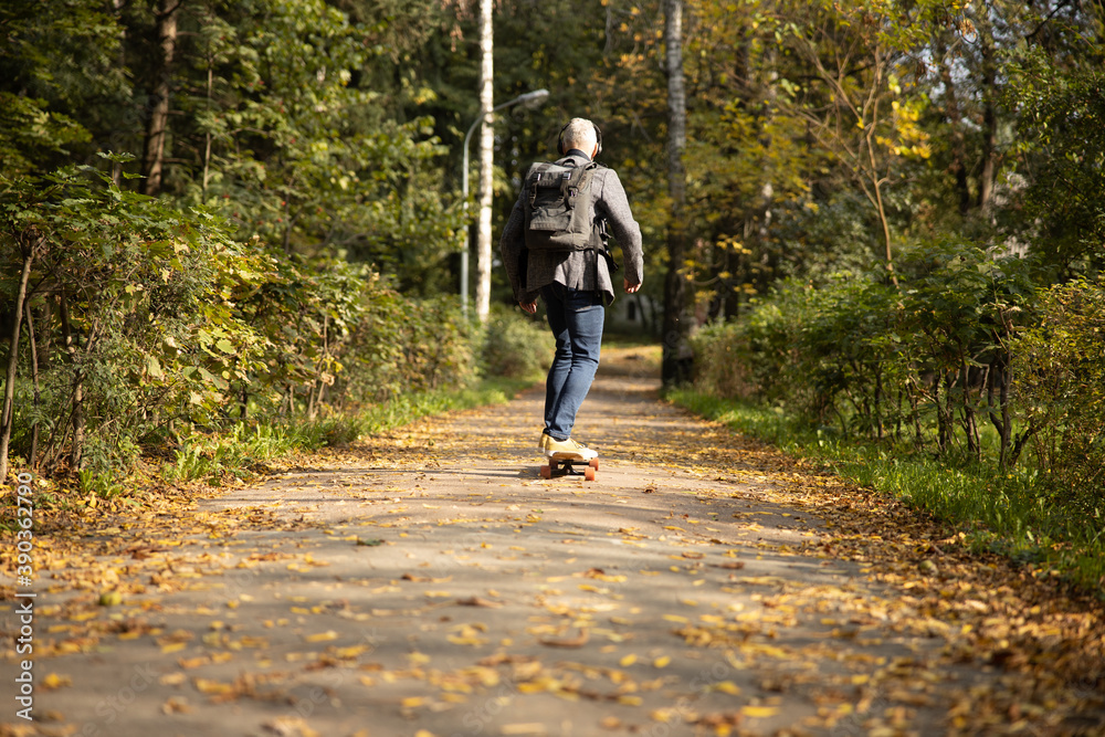 Fototapeta premium Mature man in headphones skateboarding in wood