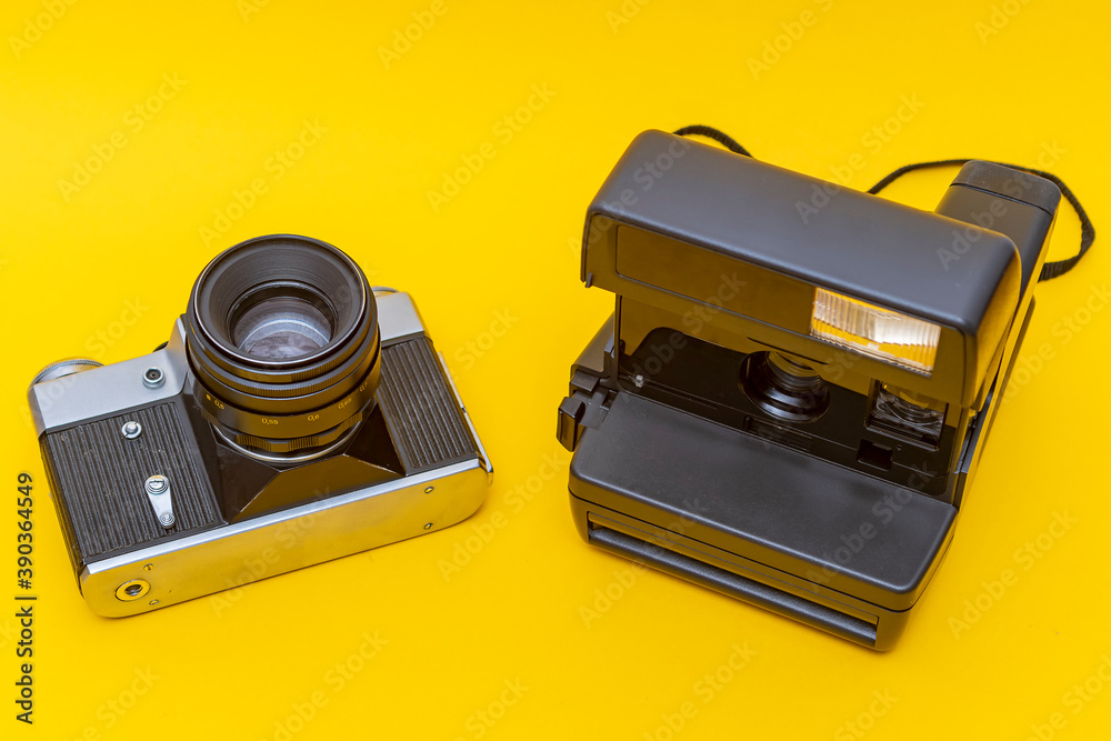 Two discontinued cameras, film and instant photography, stand against a yellow background Two discontinued cameras, film and instant photography, stand against a yellow background