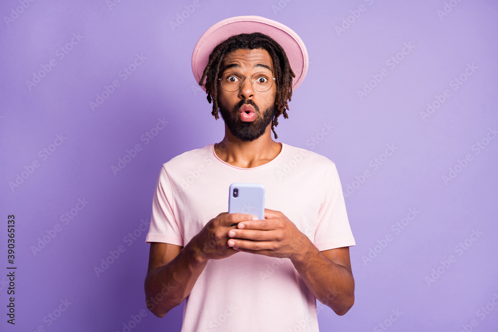 Photo portrait of shocked man in pink hat holding phone in two hands isolated on vivid purple colored background Photo portrait of shocked man in pink hat holding phone in two hands isolated on vivid purple colored background