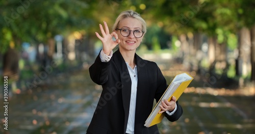 A beautiful girl in glasses and with a yellow folder in her hand shows to the camera with her hand 