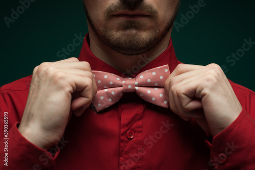 Fototapete Close-up of the hands of a young man in a red shirt correcting bow-tie against a green background