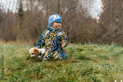 cute little caucasian girl holding a toy dog sitting on grass in countryside