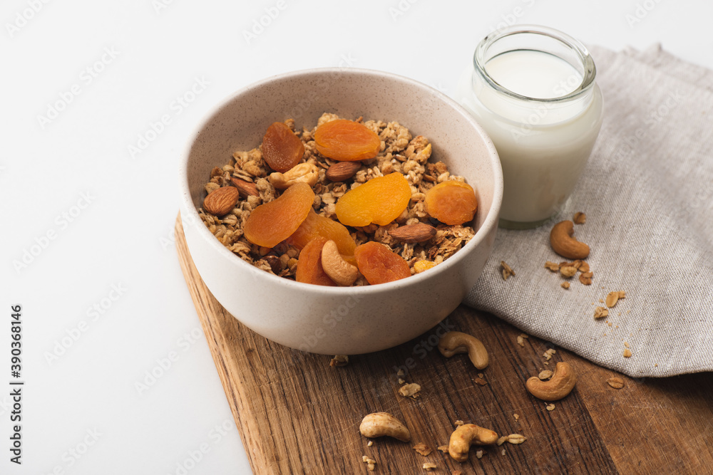 delicious granola with nuts, dried apricots and yogurt on wooden board on white background delicious granola with nuts, dried apricots and yogurt on wooden board on white background