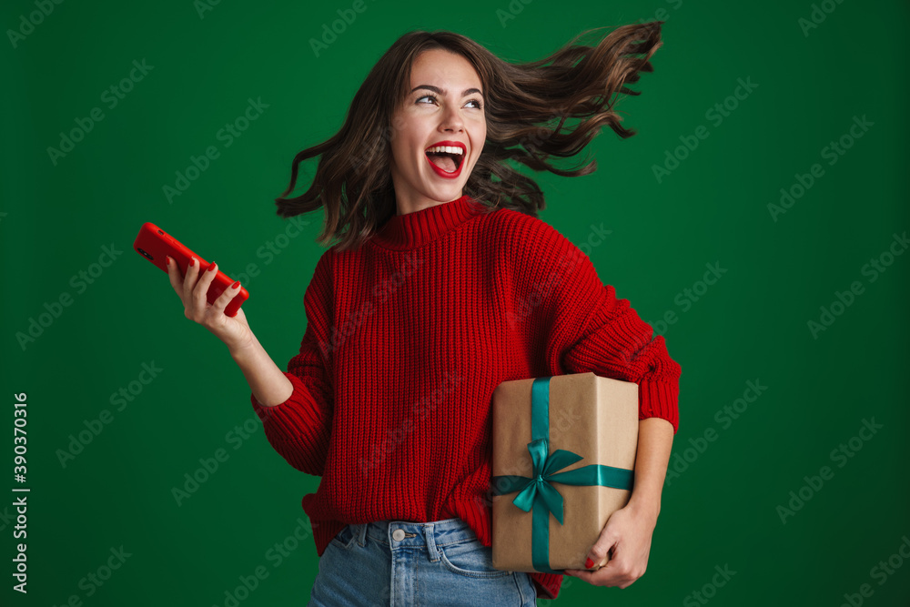 Φωτογραφία Excited girl screaming while posing with Christmas gift and cellphone