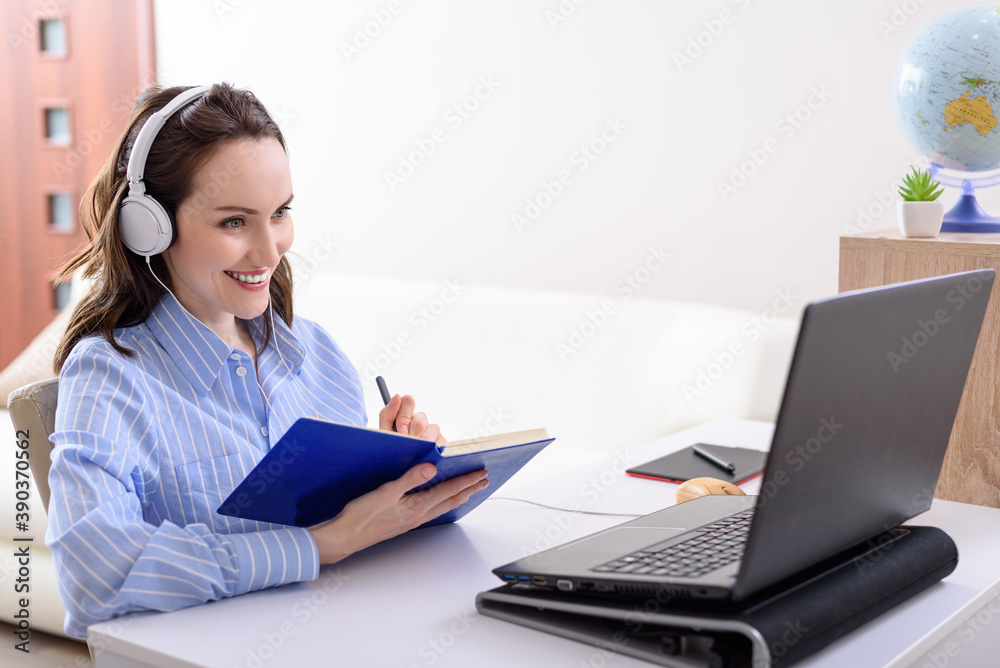 young smiling girl in blue shirt with headphones sitting at laptop, online courses, e-learning young smiling girl in blue shirt with headphones sitting at laptop, online courses, e-learning
