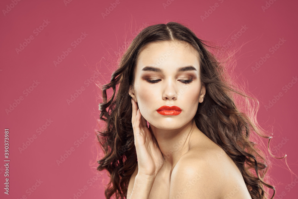 Beautiful brunette woman with makeup on her face on a pink background naked shoulders