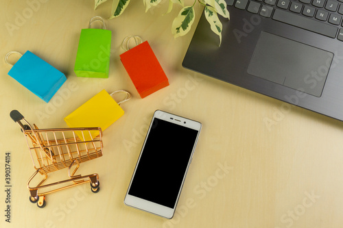 online shopping concept. little deliver boxes, smartphone, shopping bags, shopping bascket stand on laptop. copy space