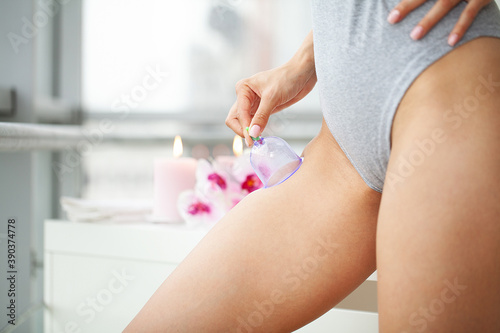 Woman getting anti-cellulite massage of hips with use of vacuum cans in beauty studio
