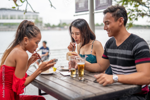 Three asian friends enjoying outdoor time seated at a restaurant table
