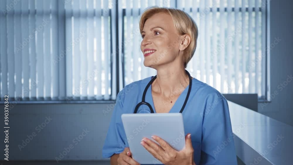 middle aged doctor using digital tablet and smiling while looking away middle aged doctor using digital tablet and smiling while looking away