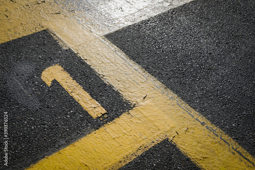 sign on the asphalt, yellow painted number one on grey street, yellow lines like a corner on the road, 
space for text 