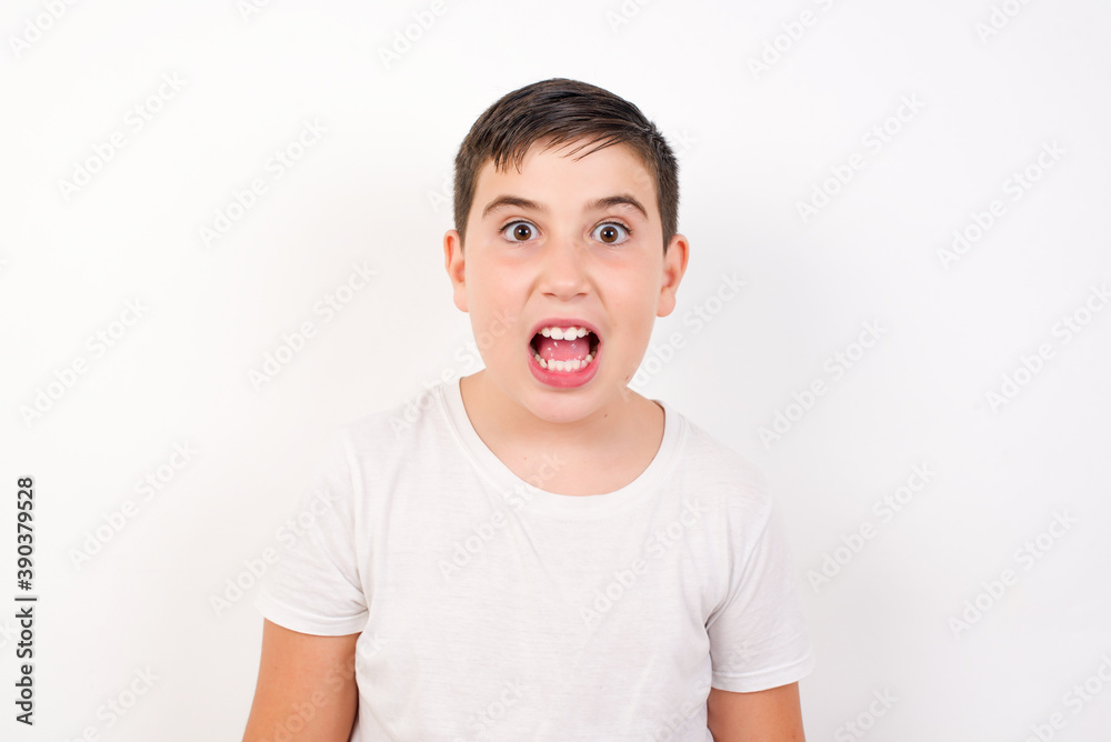 Caucasian young boy standing against white background  having stunned and shocked look, with mouth open and jaw dropped exclaiming: Wow, I can't believe this. Surprise and shock