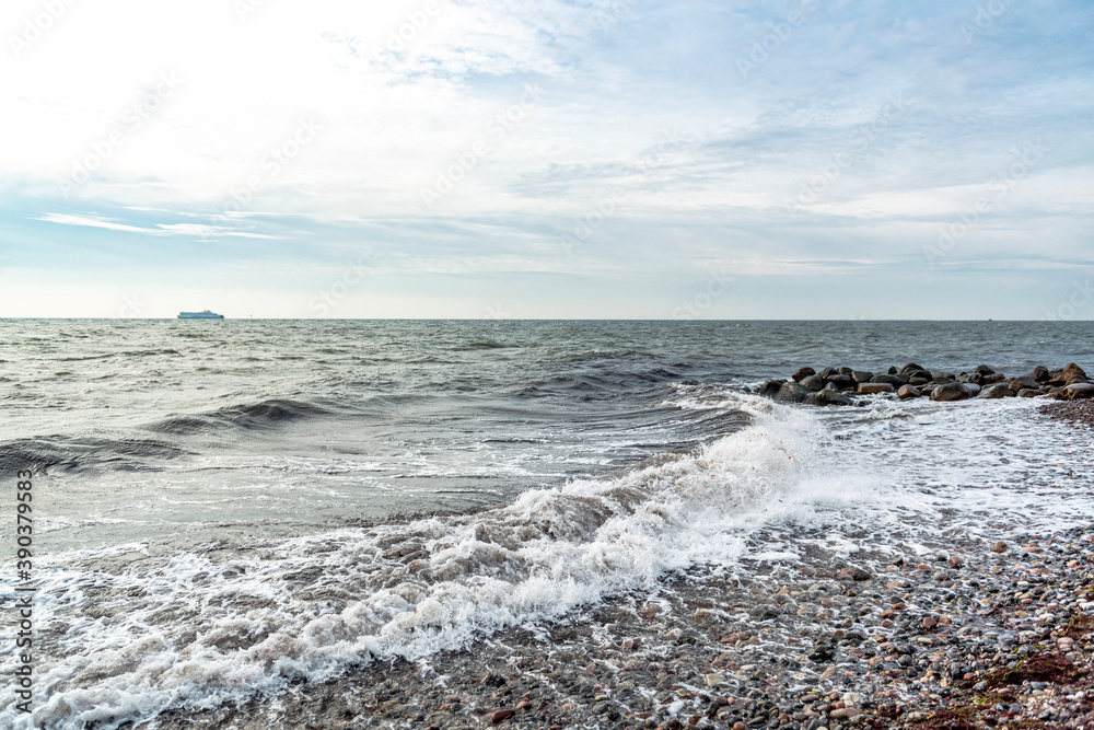 Wellen treffen auf den Ostseestrand und die Wellenbrecher. Am Horizont fährt ein Schiff. Wellen treffen auf den Ostseestrand und die Wellenbrecher. Am Horizont fährt ein Schiff.