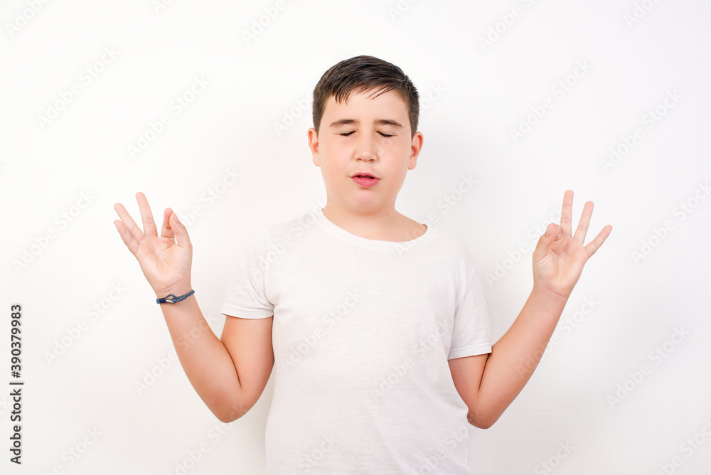 Caucasian young boy standing against white background doing yoga, keeping eyes closed, holding fingers in mudra gesture. Meditation, religion and spiritual practices. Caucasian young boy standing against white background doing yoga, keeping eyes closed, holding fingers in mudra gesture. Meditation, religion and spiritual practices.