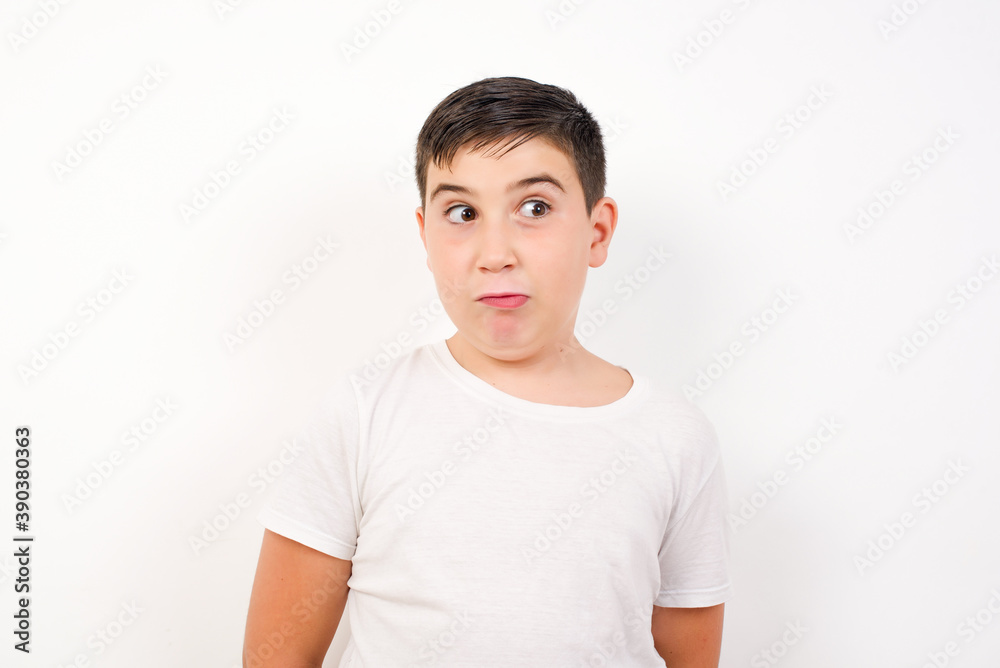 Caucasian young boy standing against white background crosses eyes, puts lips, makes grimace with awkward expression has fun alone, plays fool. Caucasian young boy standing against white background crosses eyes, puts lips, makes grimace with awkward expression has fun alone, plays fool.
