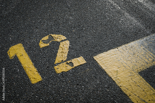 sign on the asphalt, yellow painted number twelve on grey street, yellow lines like a corner on the road, space for text 