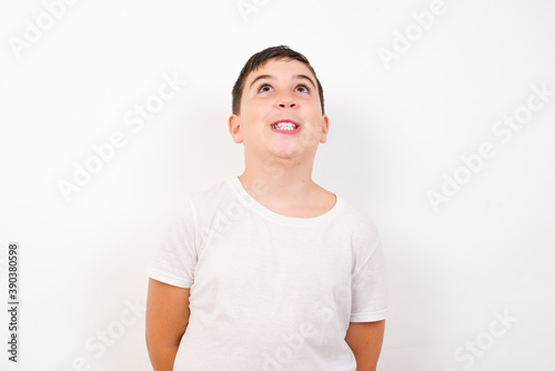 Cuadro en lienzo Portrait of mysterious Caucasian young boy standing against white background looking up with enigmatic smile