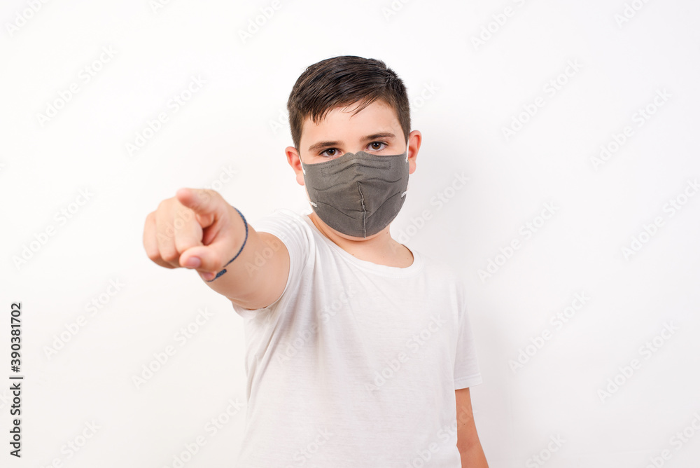Cheerful Caucasian young boy wearing medical mask standing against white background indicates happily at you, chooses to compete, has positive expression, makes choice. Cheerful Caucasian young boy wearing medical mask standing against white background indicates happily at you, chooses to compete, has positive expression, makes choice.