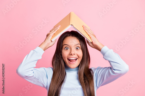 Close-up portrait of lovely overjoyed cheerful girl holding book over head having fun isolated over pink pastel color background