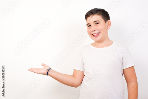 Positive glad Caucasian young boy standing against white background says: wow how exciting it is, has amazed expression, shows something on blank space with open hand. Advertisement concept.