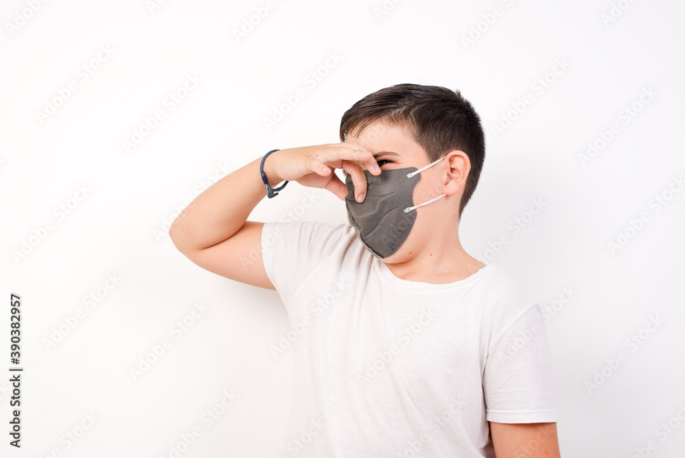 Displeased Caucasian young boy wearing medical mask standing against white background plugs nose as smells something stink and unpleasant, feels aversion, hates disgusting scent. Displeased Caucasian young boy wearing medical mask standing against white background plugs nose as smells something stink and unpleasant, feels aversion, hates disgusting scent.