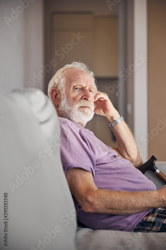 Thoughtful sad bearded male pensioner on the couch