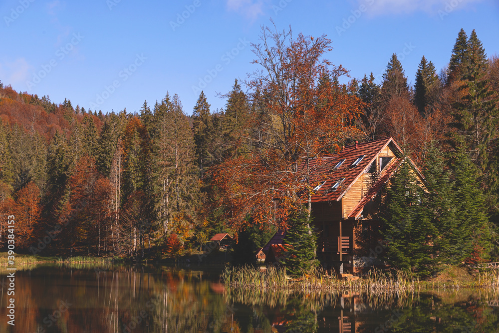 Lake in the autumn mountains among yellow and red trees with a wooden house by the water