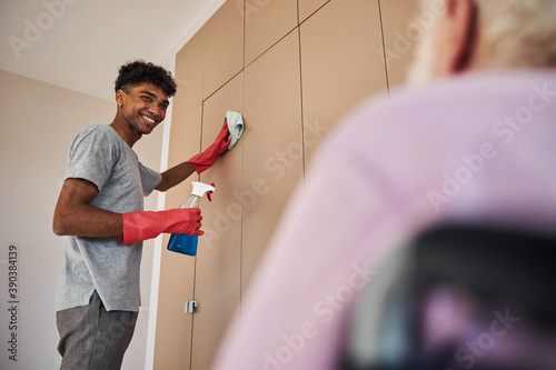 Young man helping a pensioner clean the apartment