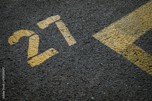 sign on the asphalt, yellow painted number twenty seven on grey street, yellow lines like a corner on the road, 
space for text 