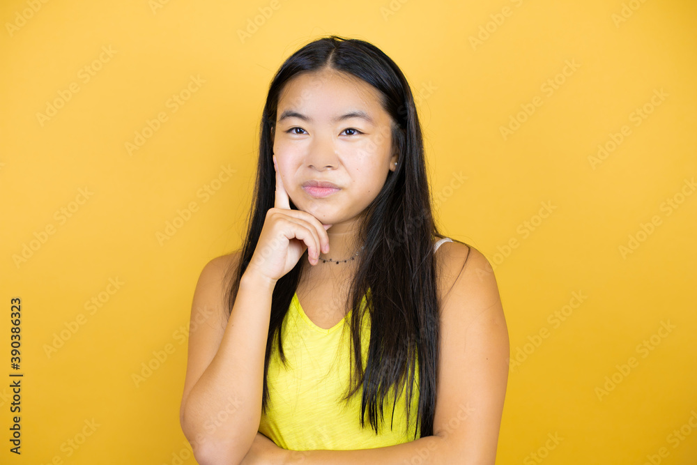 Young beautiful asian woman over yellow isolated background thinking and looking to the side Young beautiful asian woman over yellow isolated background thinking and looking to the side