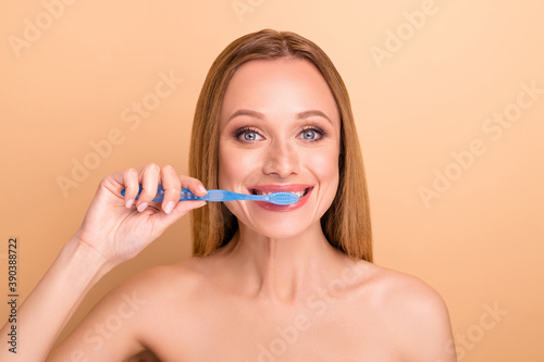 Close-up view portrait of nice-looking attractive cheerful cheery nude naked girl brushing white teeth everyday effective anti caries treatment isolated on beige pastel background
