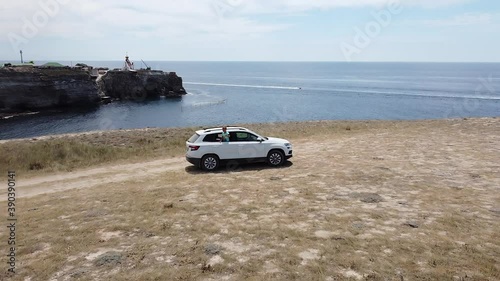 Car rides on a gravel desert road along the sea against the blue sky. The camera moves away in height tracking the car. photo