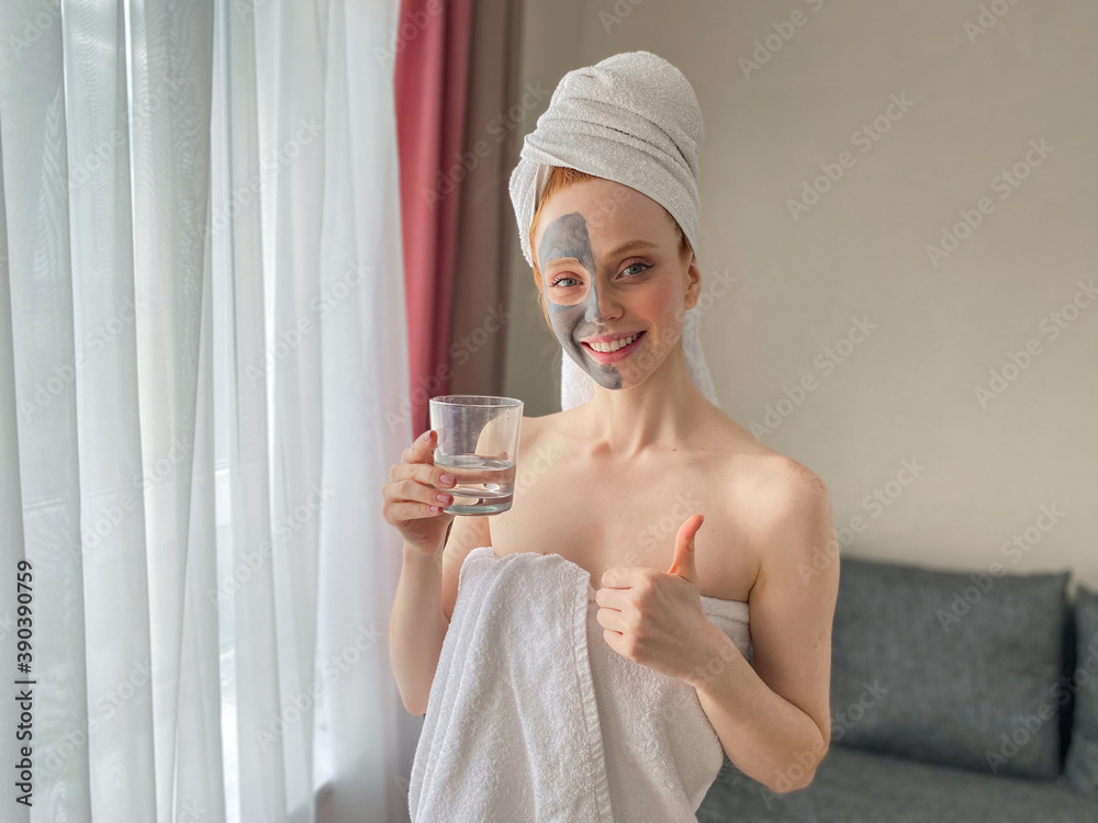 Caucasian woman applied a gray clay mask to half of her face. A woman drinks water with a clay mask on her face. Caucasian woman applied a gray clay mask to half of her face. A woman drinks water with a clay mask on her face.