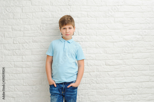 Cute stylish boy near light wall. European boy with european boy in jeans and blue shirt on light background.