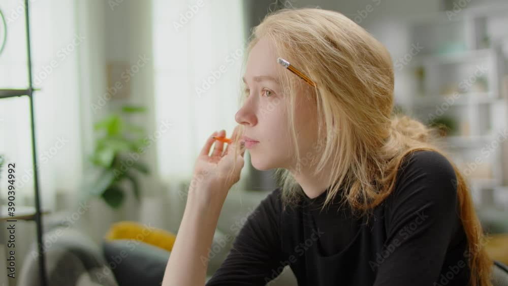 Young blonde woman dreaming while sitting at a desk at home while studying Young blonde woman dreaming while sitting at a desk at home while studying