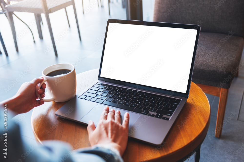 Fototapeta premium Mockup image of a hand touching on laptop computer touchpad with blank white desktop screen while drinking coffee