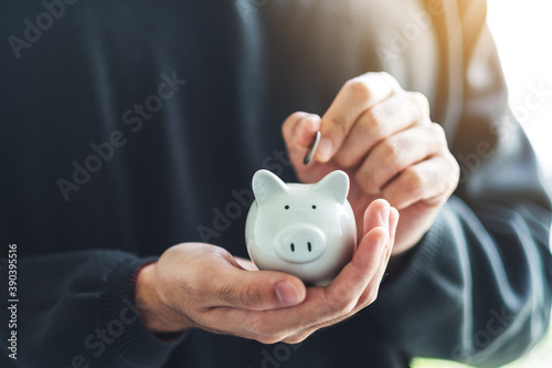 Closeup image of a man holding and putting coin into piggy bank for saving money and financial concept