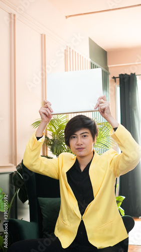 Working Asian smart woman in yellow suit holding white copy space banner in luxury interior background