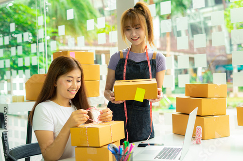 Female SME business owners and colleagues Are helping to pack products And showing a smile, happy to receive a large order from regular customers, entrepreneurial office concept Sell ​​products online © crizzystudio