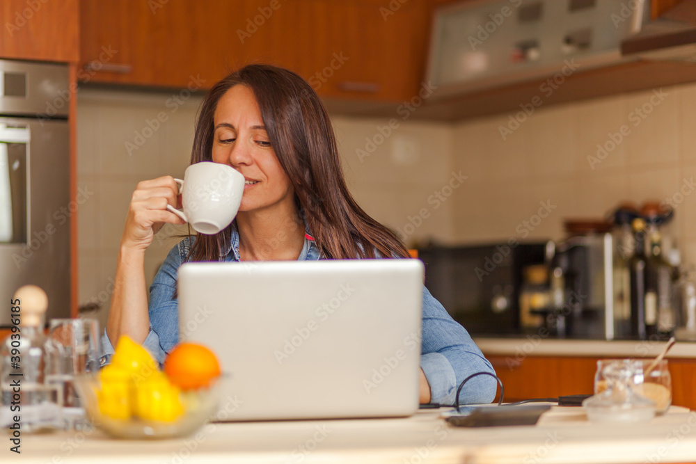 Happy woman drinking coffee and using computer in the kitchen. Happy woman drinking coffee and using computer in the kitchen.