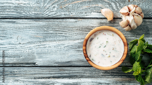 Authentic pakistani cucumber raita sauce on gray wooden background. Raita sauce dip with cucumber, onion and tomato add-ins in small metal bowl and glass jar. Top view or flat lay. Copy space. Banner photo