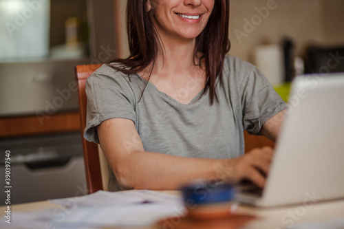 Unrecognizable woman with a smile using laptop at home.