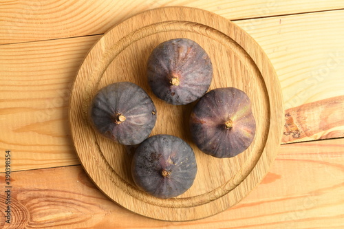 Ripe dark blue organic figs on a wooden round tray, close-up, on a wooden table.