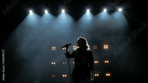 Silhouette of a girl comes to the microphone on the stage against a background of bright yellow lights