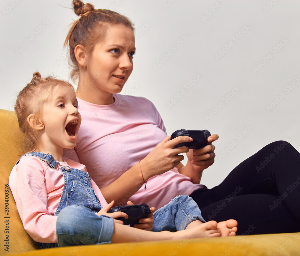 Excited young mother and cute little daughter sit on couch relax playing video games at home together, happy and small girls have fun in in living room. Excited young mother and cute little daughter sit on couch relax playing video games at home together, happy and small girls have fun in in living room.