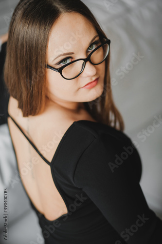 portrait of a young girl in glasses and a black dress sitting on a white sofa