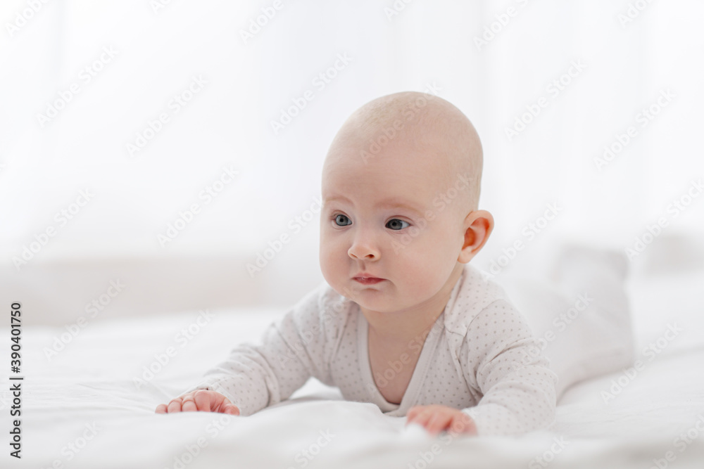 Portrait of a cute beautiful baby with gray eyes in white pajamas on the bed against the window. Portrait of a cute beautiful baby with gray eyes in white pajamas on the bed against the window.
