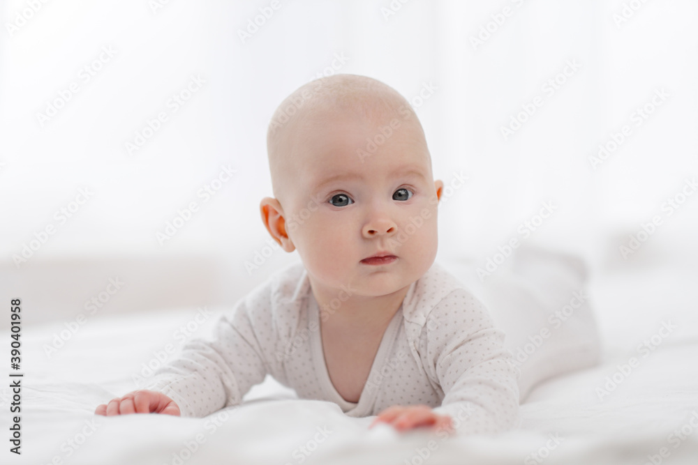 Portrait of a cute beautiful baby with gray eyes in white pajamas on the bed against the window. Portrait of a cute beautiful baby with gray eyes in white pajamas on the bed against the window.