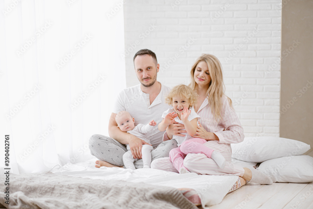 A young Caucasian family with two children daughters in a white home interior. Home clothes. A young Caucasian family with two children daughters in a white home interior. Home clothes.